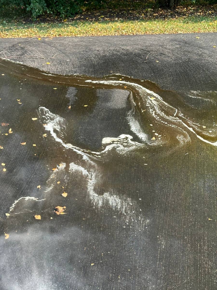 Water and cleaning runoff being rinsed down a sloped asphalt driveway at low pressure with a wide fan tip