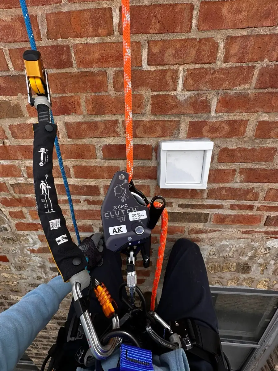 Rope access gear beside a dryer vent cover high on a brick wall in a Chicago gangway