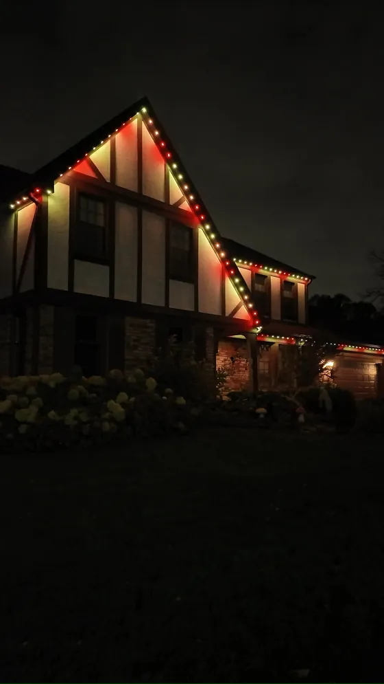 The same Tudor home with its permanent roofline lighting set to red and green for Christmas