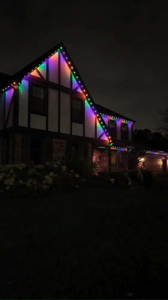 The same Tudor home with its permanent roofline lighting running a full multicolor pattern across every gable
