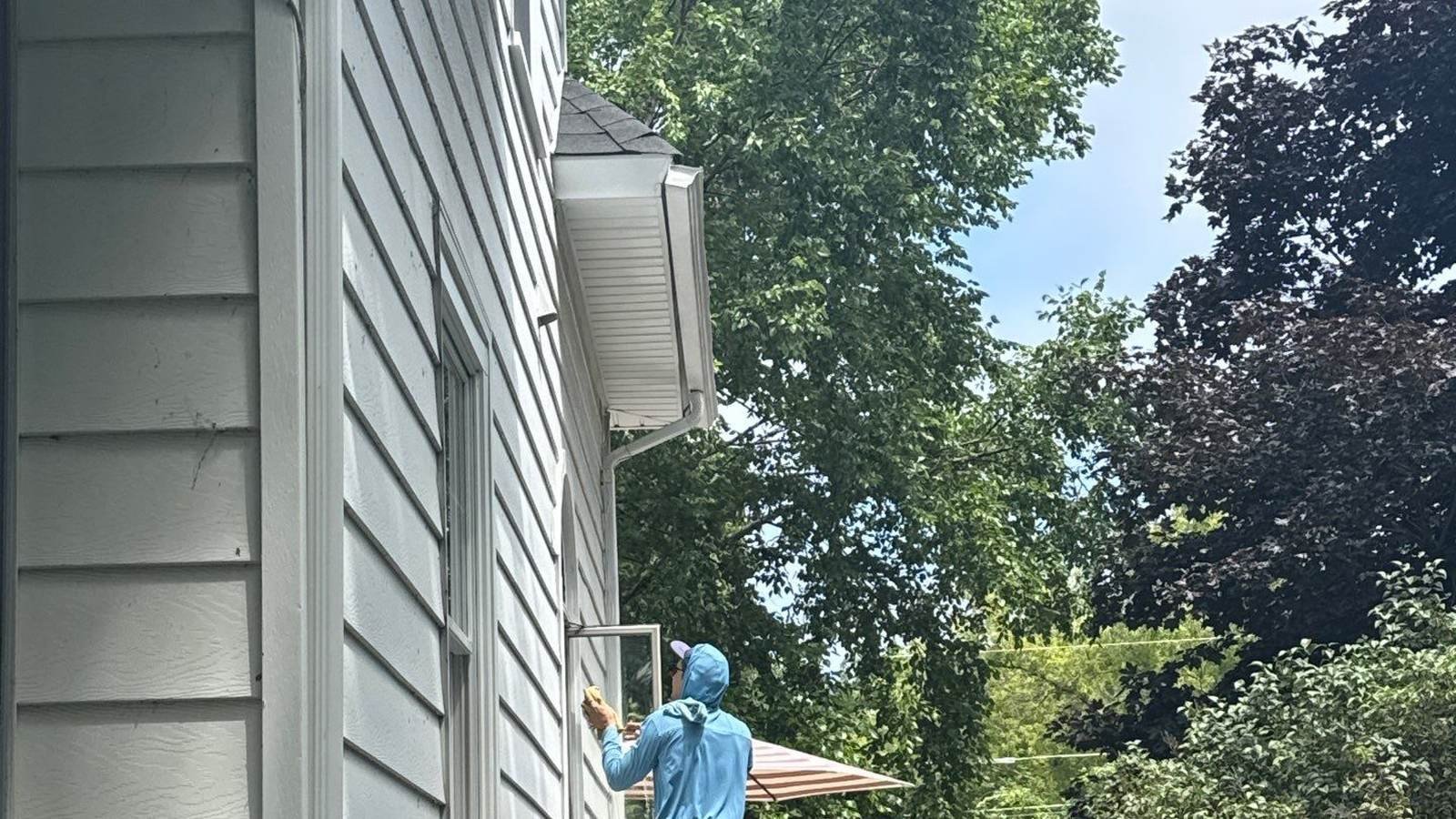 Pane Pal technician on a ladder cleaning upper story windows beside a narrow side yard